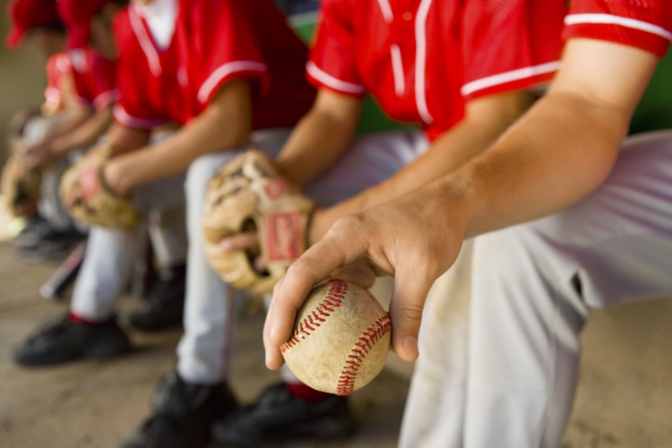 Teenage baseball players sit in the dugout together